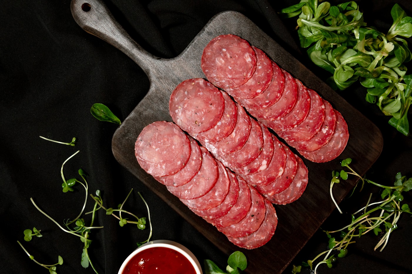 Salami rebanado sobre tabla con hierbas