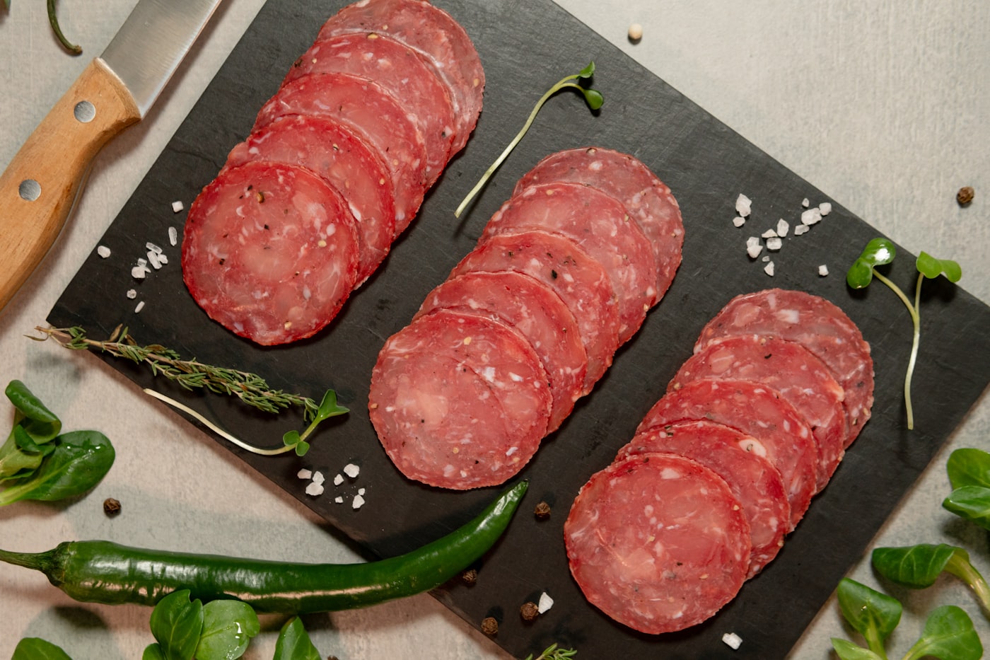 Rebanadas finas de salami dispuestas sobre tabla oscura