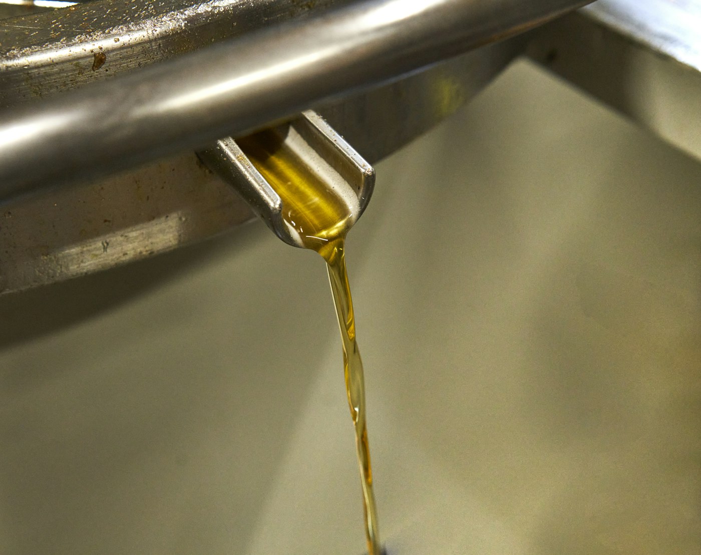 Aceite dorado vertido desde una boquilla metálica