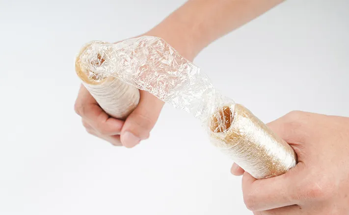 Manos estirando una tripa de celulosa transparente para mostrar su flexibilidad